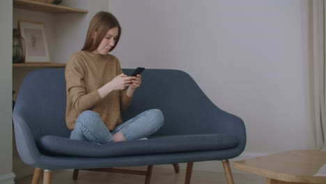 business-woman-typing-message-on-mobile-phone-at-home-office.-Young-girl-chatting-on-phone-in-slow-motion.-Close-up-young-woman-hands-using-smartphone-on-couch.